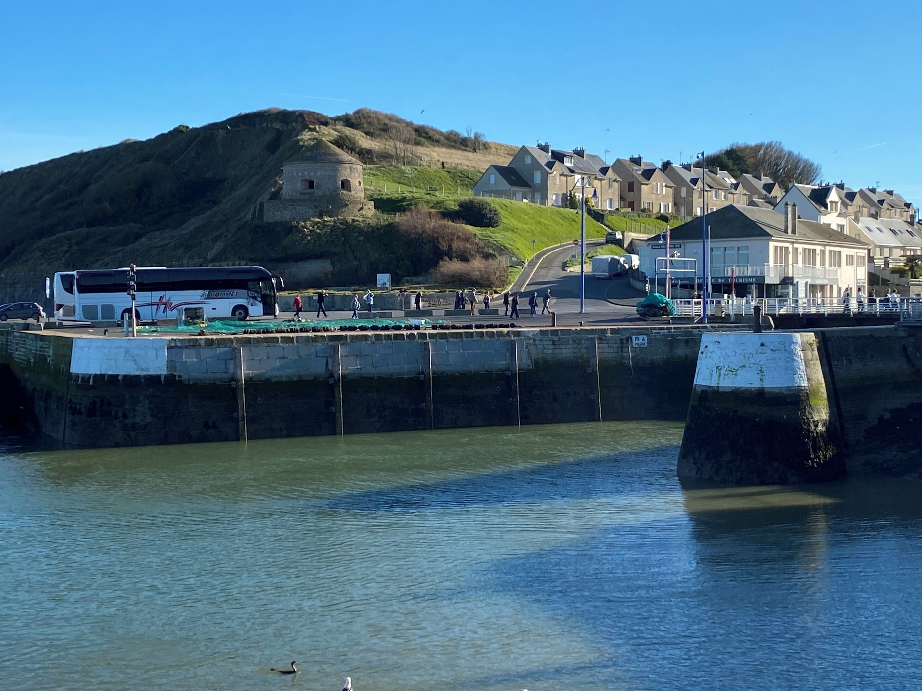 A coastal area with a bus, a stone wall, and buildings in the background.
