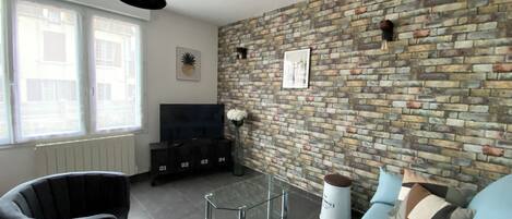 A living room with a brick wall, a sofa, a chair, a glass coffee table, and a TV stand.