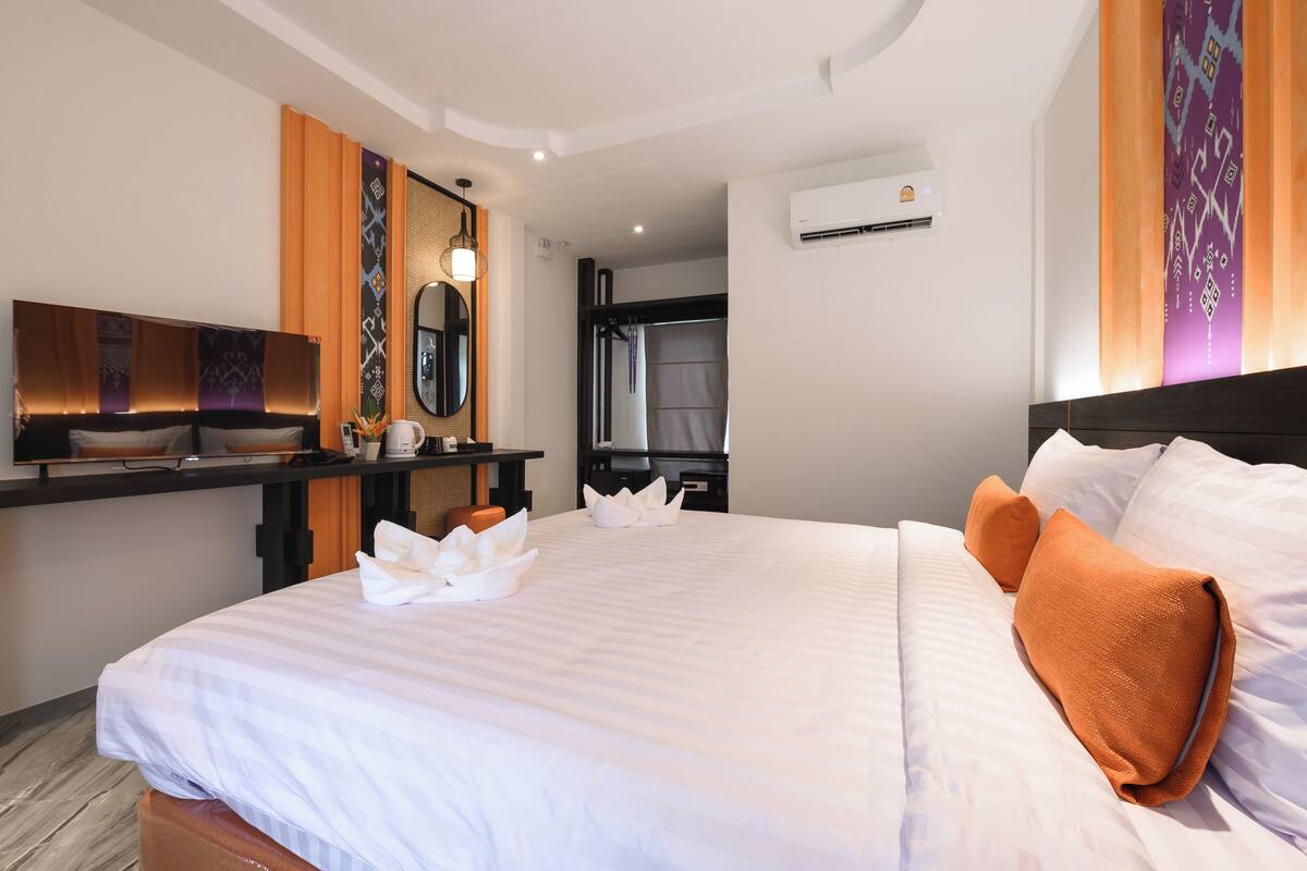 Une chambre d’hôtel avec un grand lit, un bureau doté d’un téléviseur à écran plat, un miroir et un climatiseur fixé au mur.