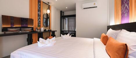 A hotel room with a large bed, a desk with a flat-screen TV, a mirror, and a wall-mounted air conditioner.