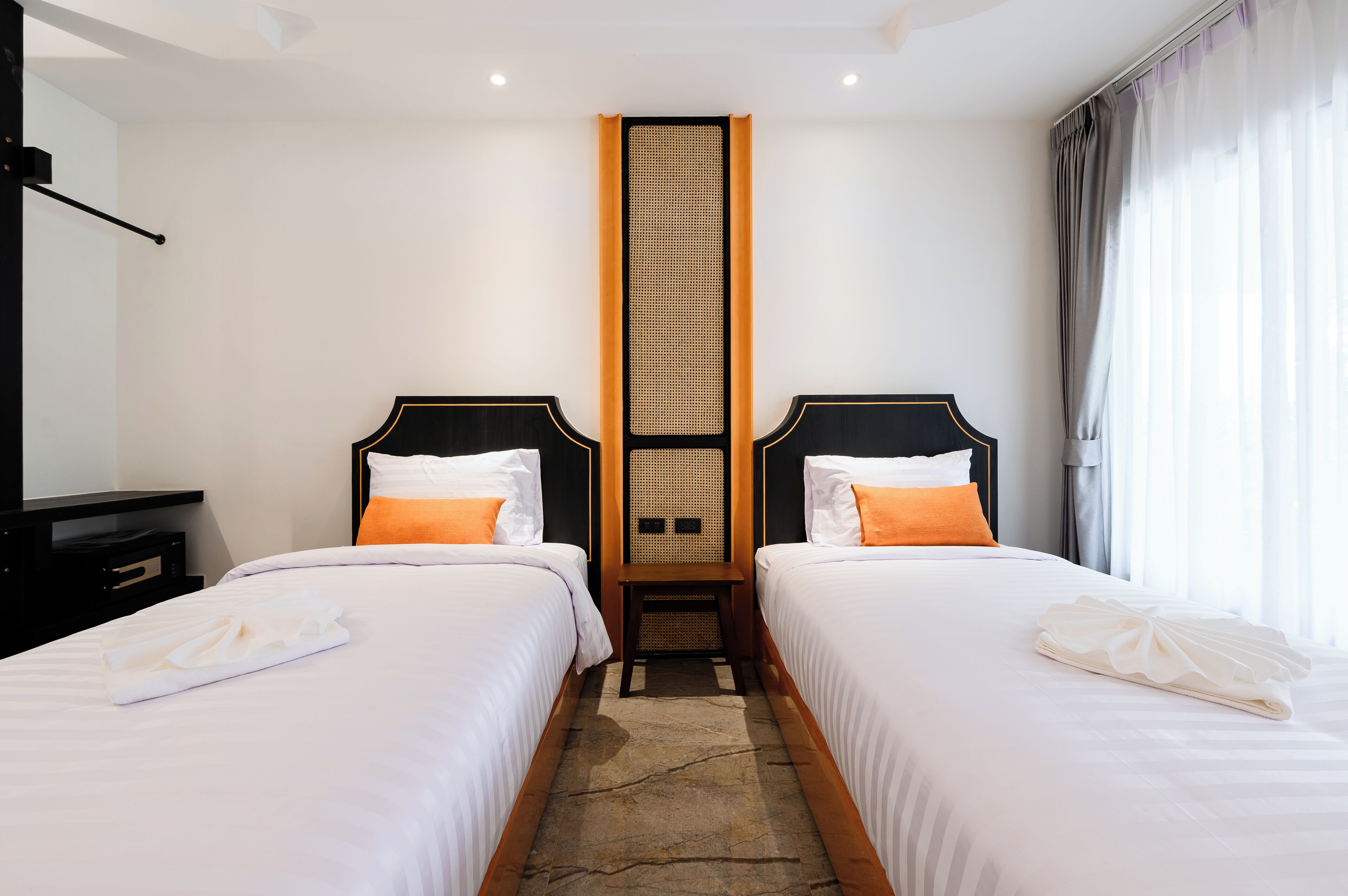 A hotel room with two beds, a central partition, and a view of the outdoors.