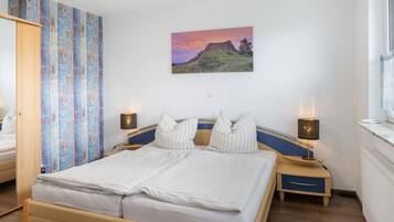 A bedroom with a bed, two bedside tables, a nightstand, a wall-mounted lamp, and a painting.