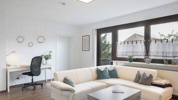 Ett modernt vardagsrum med en vit soffa, ett skrivbord och ett fönster med gardiner.