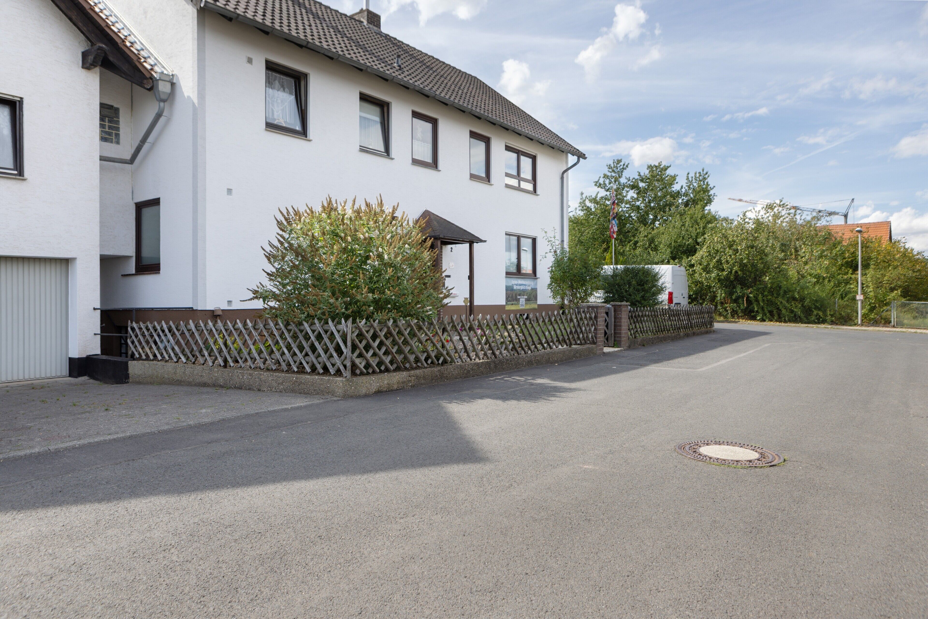 Ein zweistöckiges Wohnhaus mit weißer Fassade, einem Ziegeldach und einer umzäunten Auffahrt.