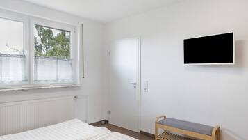 Ett sovrum med en säng, en bänk, en tv, en dörr och ett fönster.