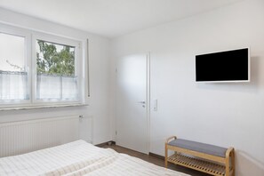 A bedroom with a bed, a bench, a TV, a door, and a window. - Apartment 'Helfensteinblick' with Mountain View, Balcony and Wi-Fi (Calden)