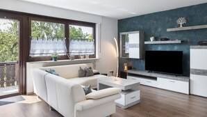 A modern living room with a sofa, coffee table, TV, and a large window with curtains.