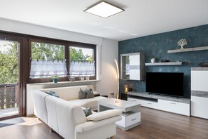 Un saló modern amb un sofà, una taula de centre, un televisor i una finestra gran amb cortines.