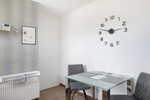 Een moderne kamer met een glazen tafel, twee stoelen, een wandklok, een radiator en een lijst met een afbeelding.