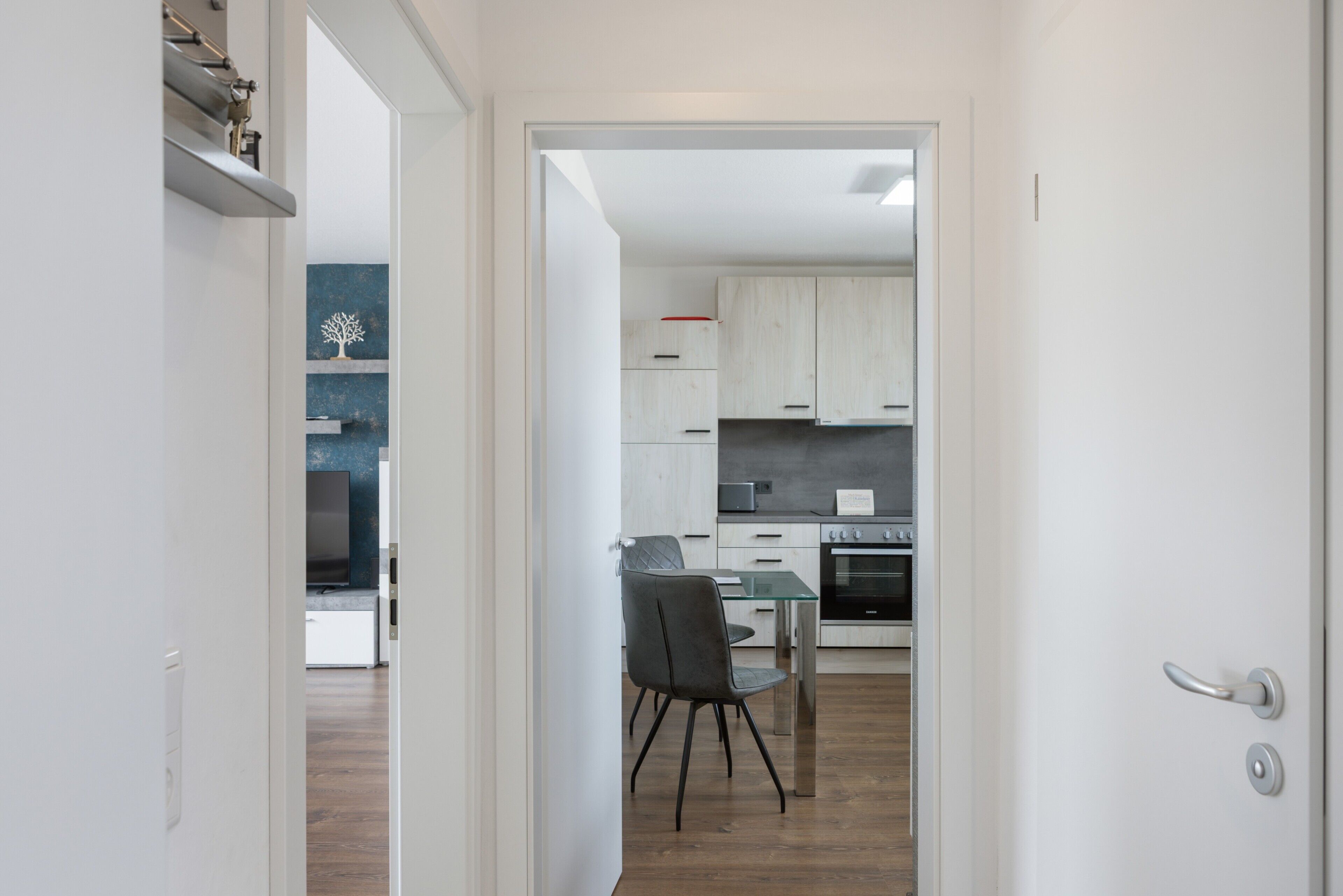 A modern kitchen with white cabinets, a built-in oven, and a dining area with a glass table and chairs.