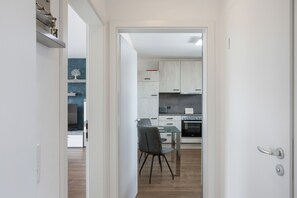 Una cuina moderna amb armaris blancs, forn integrat i zona de dinar amb taula i caires de vidre.