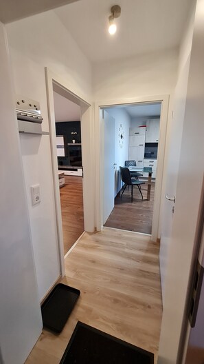 A hallway leading to a dining area with a clock on the wall, a black chair, and a small table.