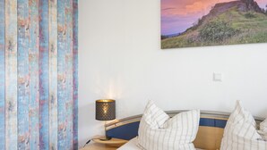 A bedroom with a bed, a nightstand, a lamp, a painting, and a window with curtains.