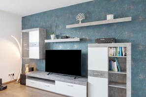 A modern living room with a flat-screen TV, built-in shelving, and a minimalist design. - Apartment 'Helfensteinblick' with Mountain View, Balcony and Wi-Fi (Calden)