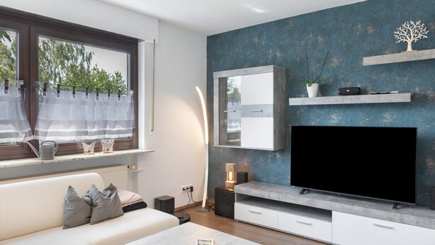 A modern living room with a large flat-screen TV, a sofa, a coffee table, and a window with curtains.