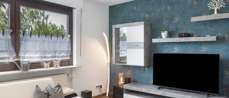 Una sala de estar moderna con una televisión de pantalla plana grande, un sofá, una mesa de centro y un ventanal con cortinas.
