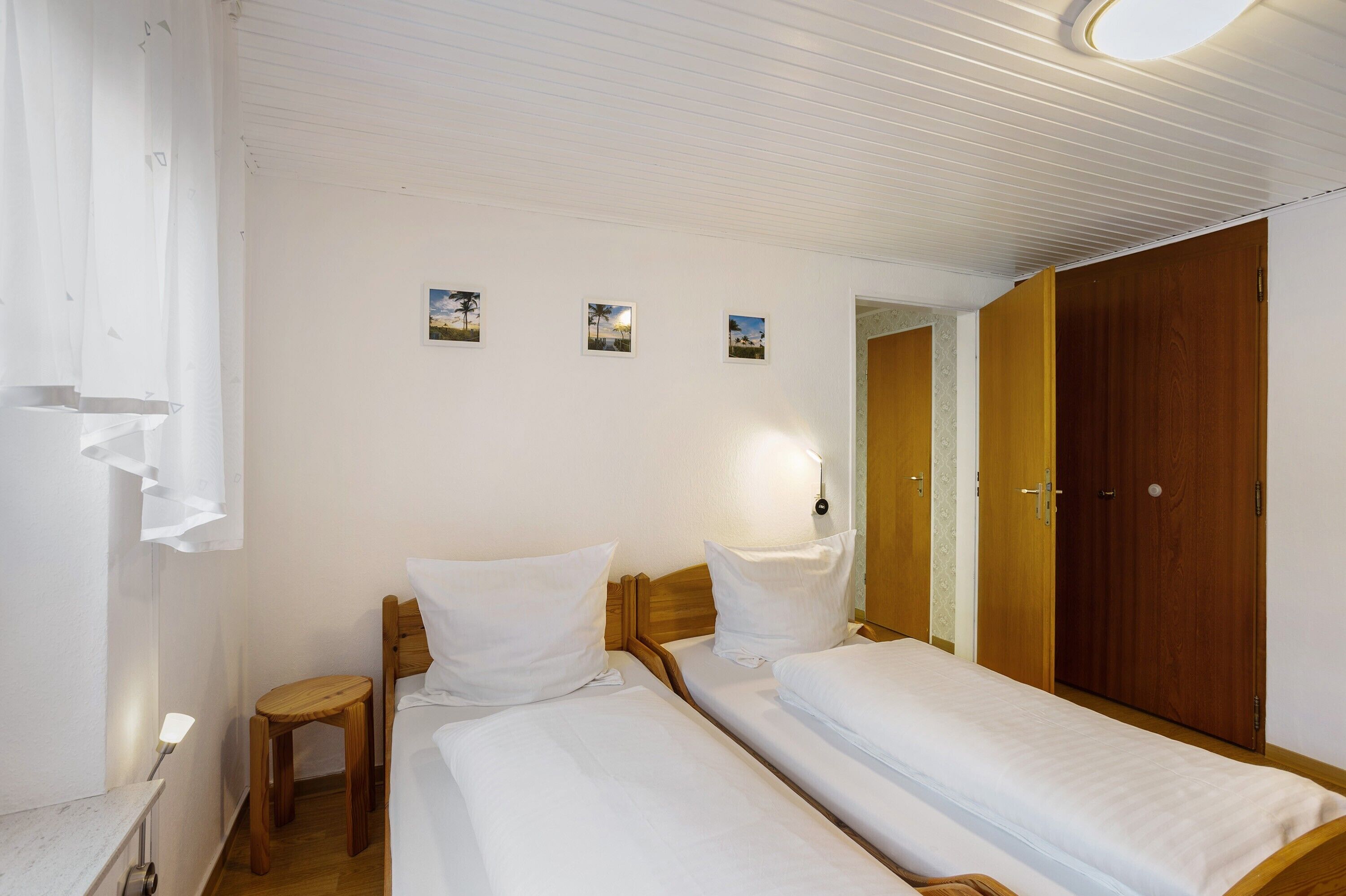 A room with two beds, a wooden wardrobe, a small table, and wall-mounted pictures.