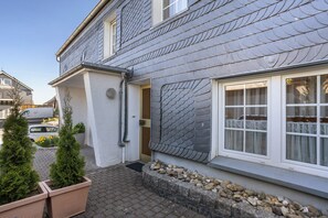 A residential building with a grey tiled roof, white exterior walls, and a window with white curtains.