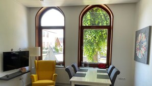 A room with a TV, a yellow armchair, a white table with chairs, large arched windows, and a painting on the wall. - Apartment 'Nickel 1' with Shared Garden and Wi-Fi (Arnis)