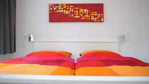 A bed with colorful bedding, a white headboard, and a red abstract painting on the wall. - Apartment 'Nickel 1' with Shared Garden and Wi-Fi (Arnis)