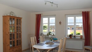 A dining area with a round table, chairs, a wooden cabinet, and a window with curtains. - Holiday Home 'Ferienhaus Stie Tinningstedt' with Private Terrace, Private Garden and Wi-Fi (Tinningstedt)
