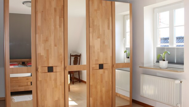 A room with a sliding wooden wardrobe, a radiator, a window with blinds, and a small plant on the windowsill. - Holiday Home 'Ferienhaus Stie Tinningstedt' with Private Terrace, Private Garden and Wi-Fi (Tinningstedt)