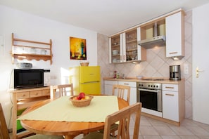 A compact kitchen with a dining table, chairs, a microwave, a yellow refrigerator, a stove, and cabinets.