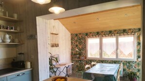 A kitchen with wooden cabinets, a dining table with chairs, and a window with a view of palm trees. - Gîte at the gateway to the Morvan (Magnien)