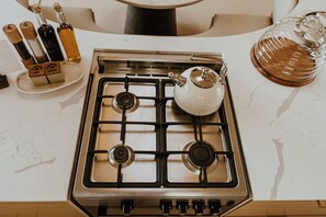 A kitchen with a gas stove, a teapot, and a glass container on the countertop.