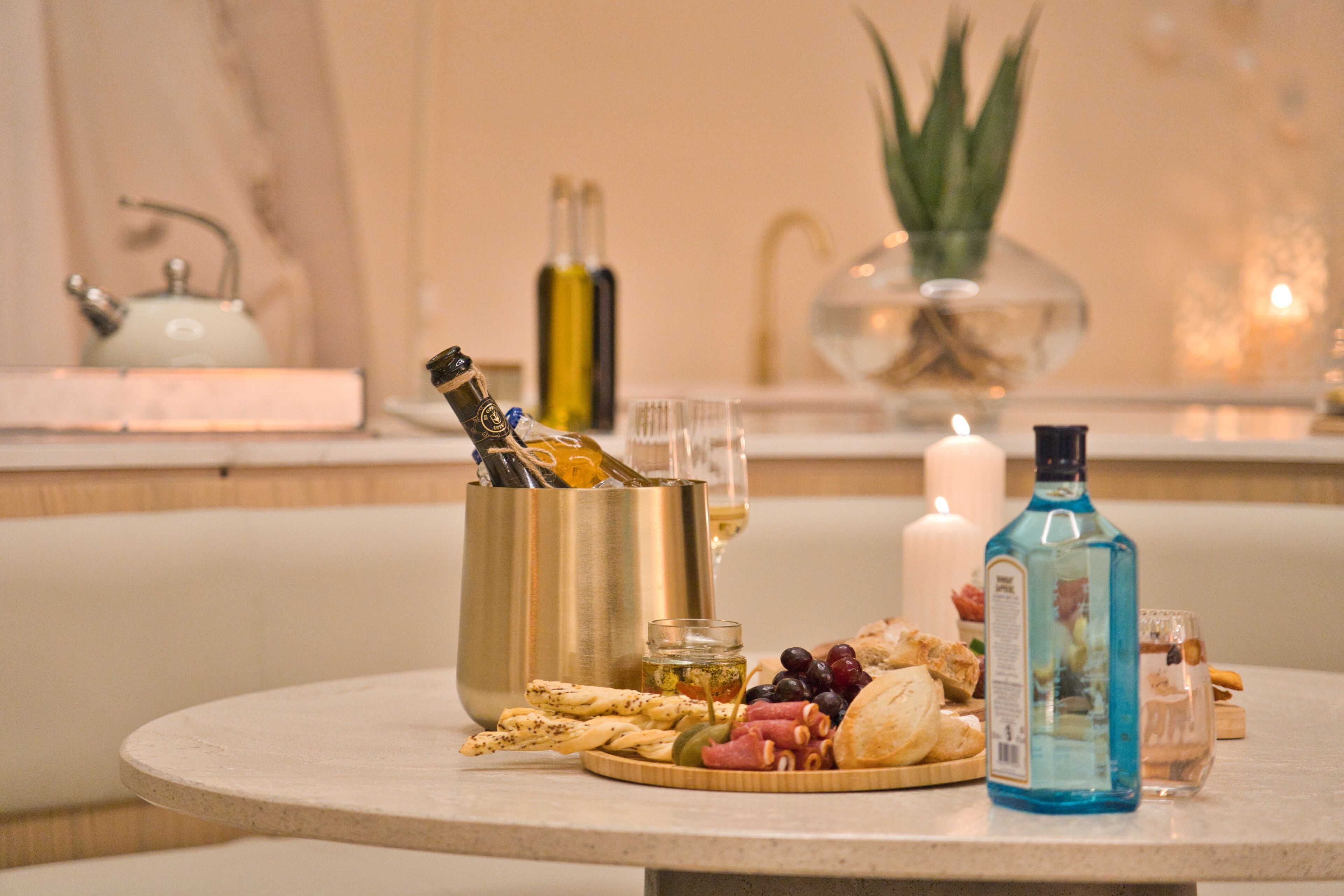 A round table with a variety of food items, including bread, olives, and cheese, and a bottle of blue liquor.
