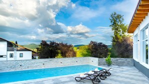 A swimming pool with lounge chairs, a stone wall, and a view of the countryside. - Holiday Home 'Bungalow 21' with Shared Garden and Wi-Fi (Dipperz)
