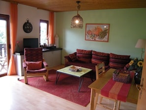 Ein Wohnzimmer mit einer Couch, Sesseln, einem Couchtisch und einem Esstisch mit einer Vase voller Sonnenblumen.