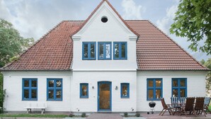 Ein zweistöckiges weißes Haus mit rotem Ziegeldach, einer Veranda mit einer Bank und einem Grill.