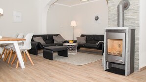 Ein modernes Wohnzimmer mit Essbereich, einer Sofagarnitur, einem Couchtisch und einem Kaminofen.