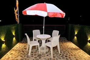 A patio with a round table and four chairs, an umbrella, and decorative lights. - Hotel Geet Palace (Varanasi)