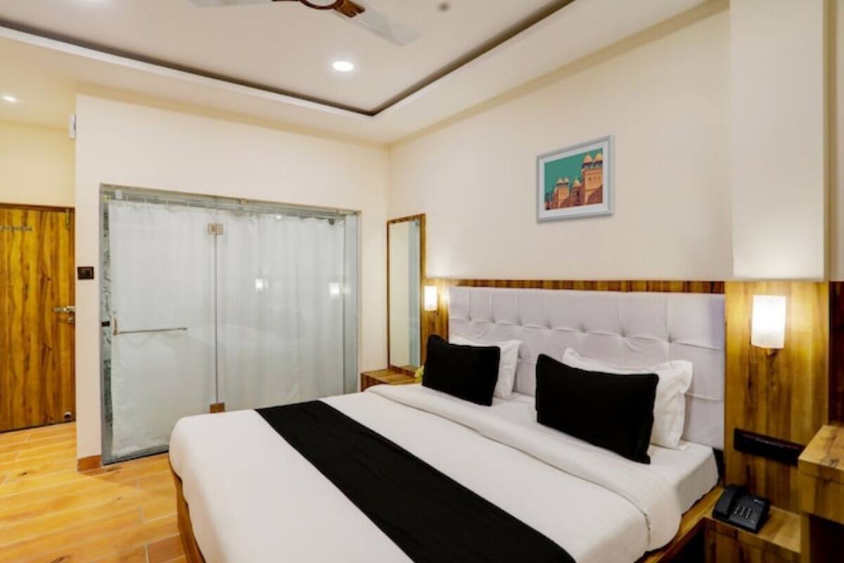 A hotel room with a large bed, a wooden headboard, a bedside table with a lamp, and a door with a curtain.
