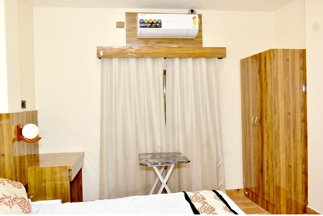 A bedroom with a bed, a small table, an air conditioning unit, and a wooden wardrobe.