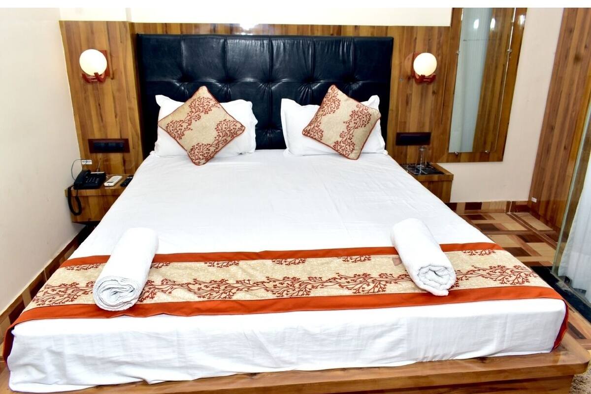 A neatly made bed with a white and orange bedspread, two decorative pillows, and a wooden headboard.