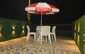 An outdoor patio with a table and chairs, an umbrella, and wall-mounted lights. - Hotel Geet Palace (Varanasi)
