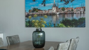 Una mesa de comedor con un florero, sillas y un cuadro con una vista urbana.