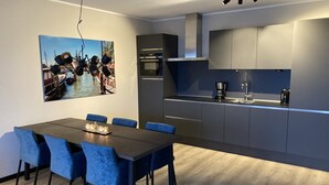 A modern kitchen with a dining area, featuring a large table with chairs, a painting of a boat on the wall, and built-in appliances. - Apartment 'Winterberg E2' with Mountain View, Shared Garden and Wi-Fi (Winterberg)