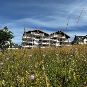 Un edificio de varios pisos con balcones, rodeado por un campo de flores silvestres y hierba.