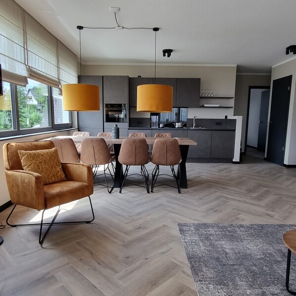 Una cocina moderna con luces colgantes, un rincón comedor con sofá y sillas, y un piso de madera con diseño espiga.