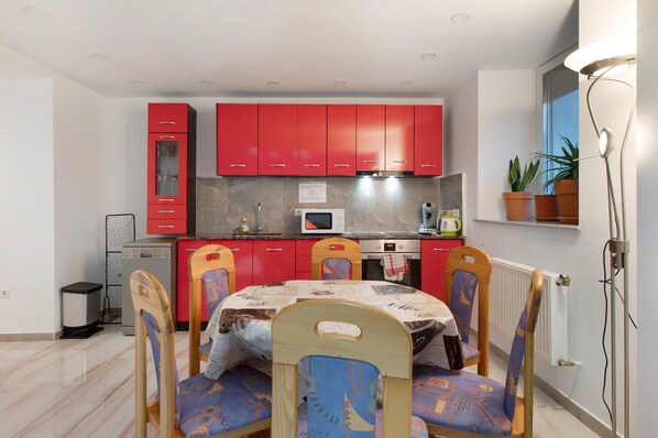 Una cocina compacta con armarios rojos, un microondas y una zona de comedor con mesa y sillas.
