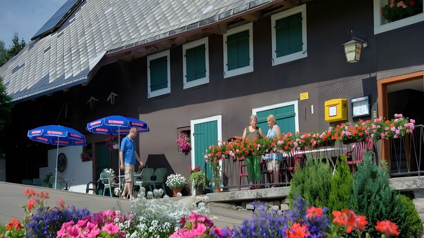 A building with a sloped roof, multiple windows, outdoor seating, and flower arrangements.