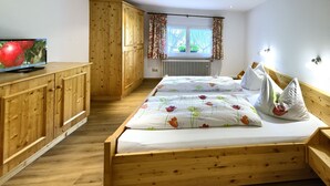 A bedroom with a wooden bed, a television on a cabinet, and a window with curtains.