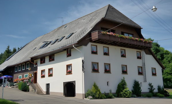 Ein mehrstöckiges Gebäude mit einem geneigten Dach, zahlreichen Fenstern und einem Balkon mit Blumenkästen.