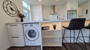 A compact kitchen with a built-in washer, white cabinetry, a clock, and a bar stool. - Stunning Views, 2 Bedroom 2 minutes to town centre (Queenstown)
