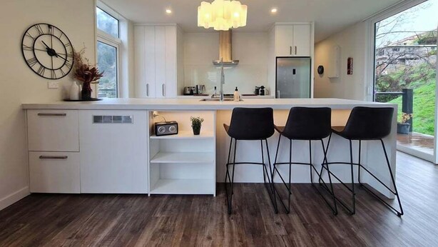 A modern kitchen with a large island, white cabinetry, a clock, and a pendant light. - Stunning Views, 2 Bedroom 2 minutes to town centre (Queenstown)