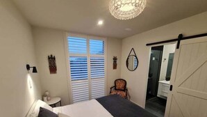 A bedroom with a large bed, a chair, a small table, a mirror, and a sliding door leading to a bathroom. - Stunning Views, 2 Bedroom 2 minutes to town centre (Queenstown)